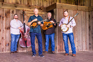 Four men standing in front of a wood wall and holding instruments.